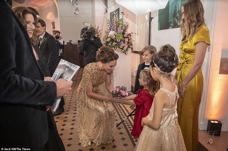 A smiling Duchess of Cambridge is presented with a gorgeous bouquet of pink flowers by a group of children at the premiere