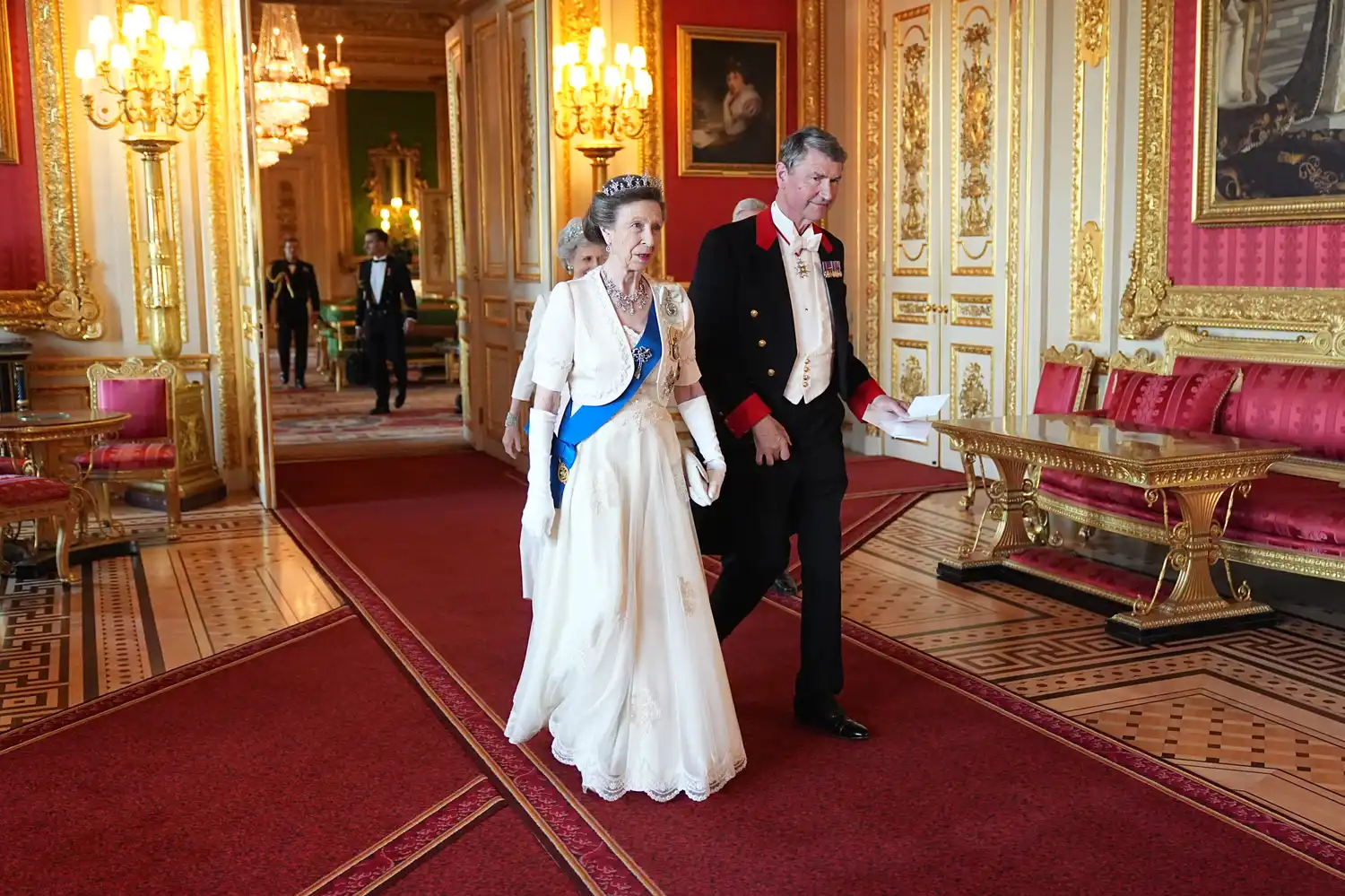 Two elderly members of the British royal family walking in an ornate room