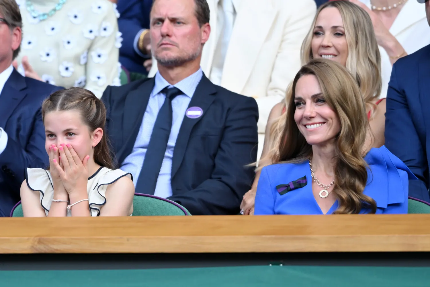 Princess Charlotte covering her mouth next to Kate Middleton smiling at an event 