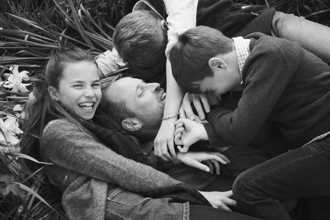 Prince George, Princess Charlotte and Prince Louis hug Prince William while laying on the grass
