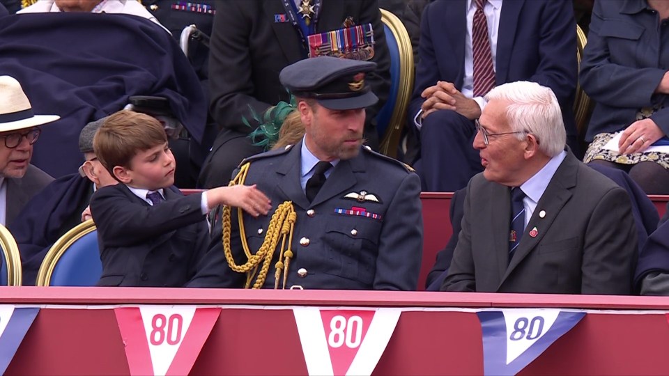 A young boy touches the epaulettes of a man in a military uniform while an older man looks on.