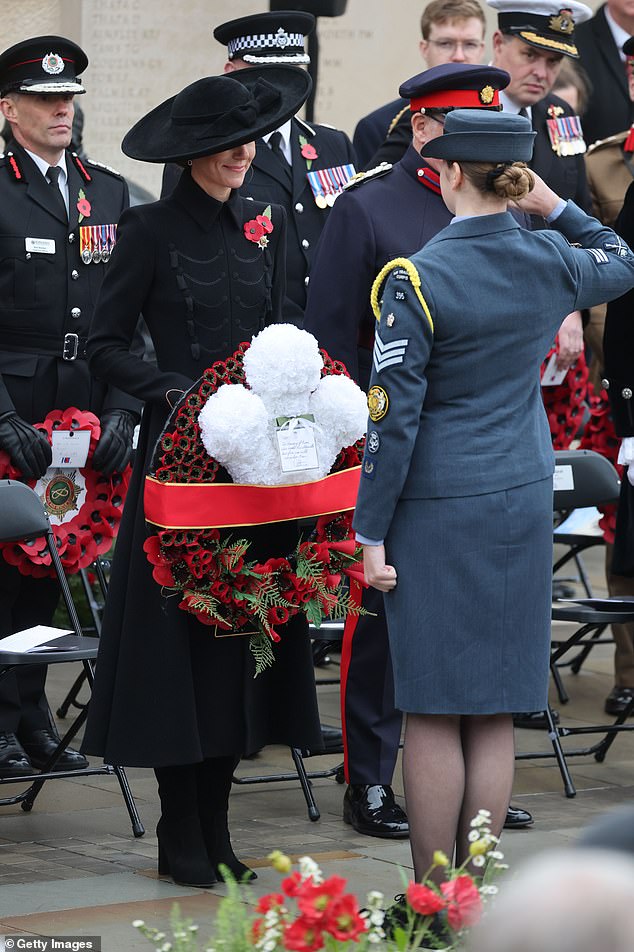 Kate smiles as she holds a wreath embellished with stunning flowers and a note she wrote to honour the fallen