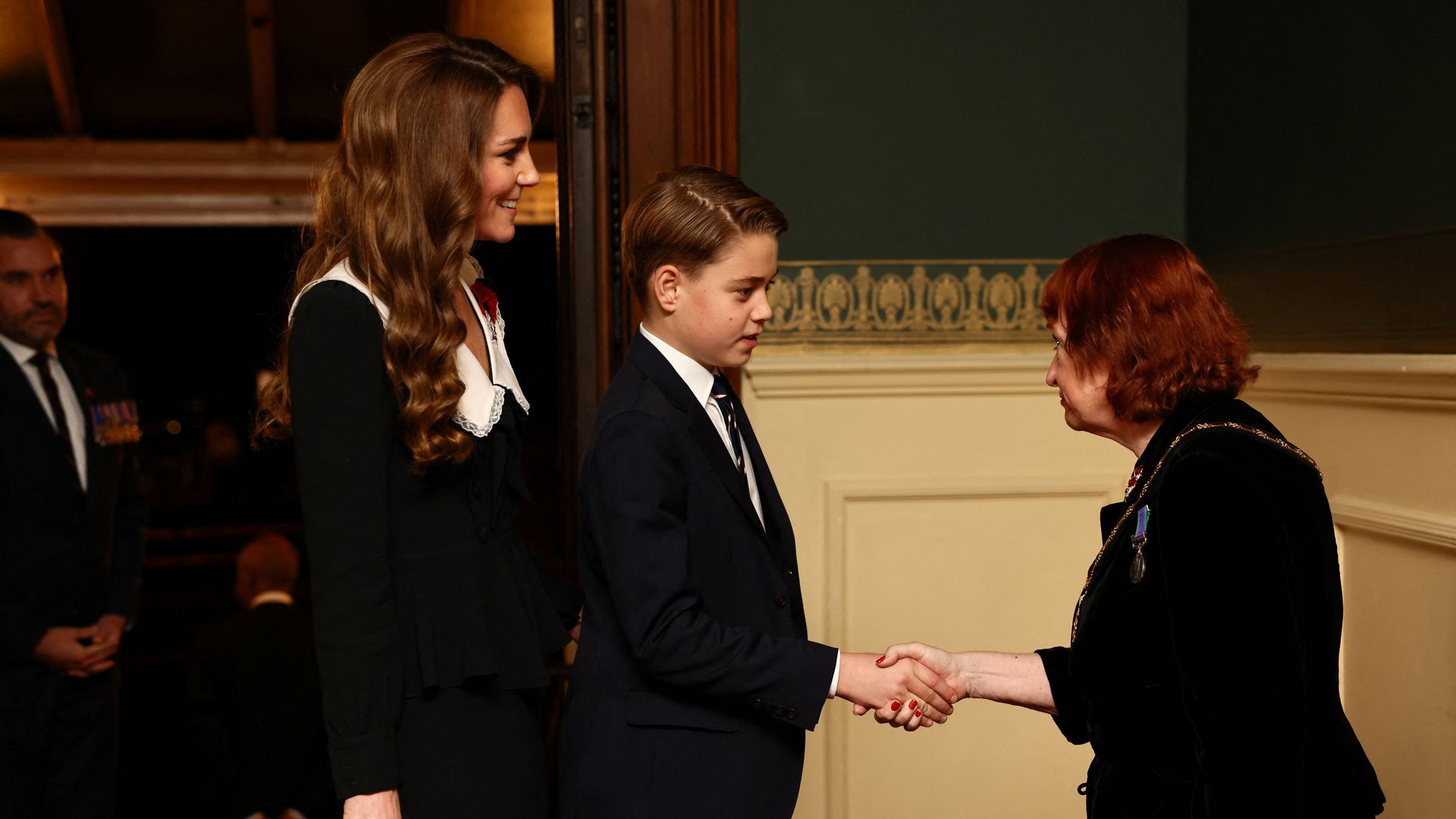 Prince George shaking hands with a woman with Kate Middleton smiling behind him