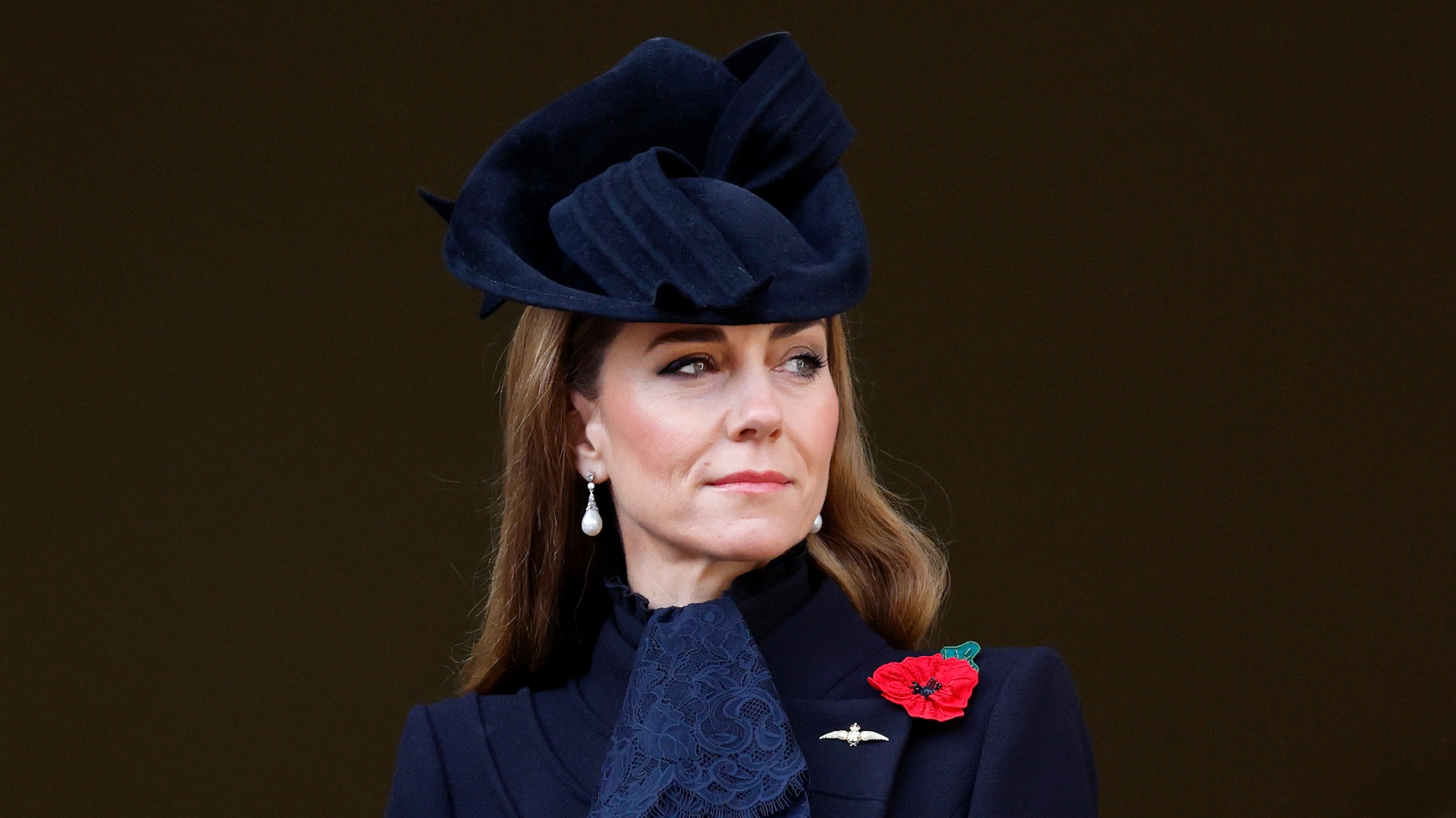 Kate Middleton wearing a black coat and hat with a red poppy pin