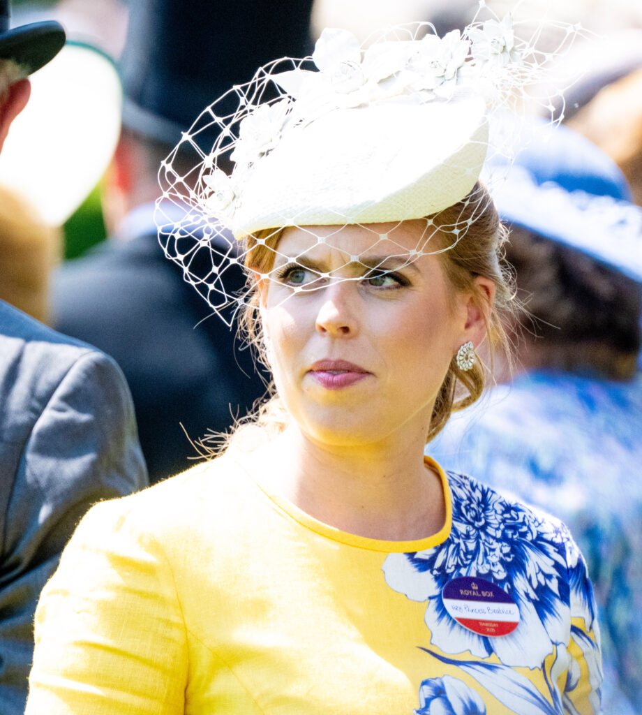 Princess Beatrice frowning wearing a white fascinator and yellow floral dress