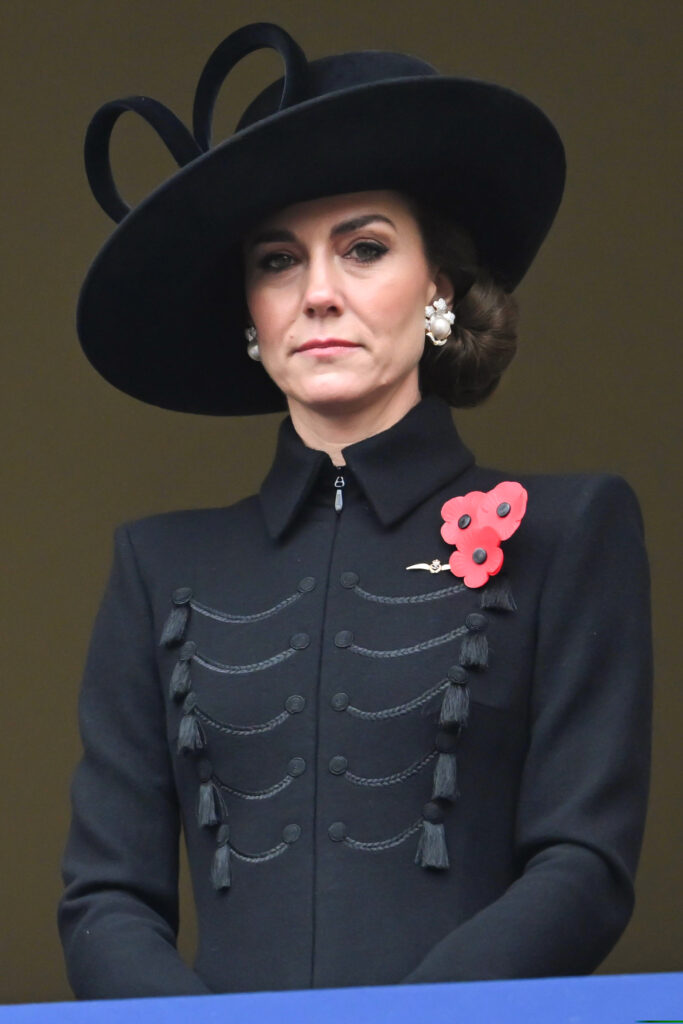 Kate Middleton wearing a black hat and a poppy and pearl earrings on Remembrance Day, looking at the camera