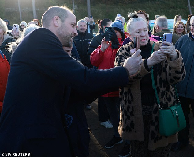 The Prince of Wales takes a selfie with a woman while on a beach walk with young people who are part of the Marine Conservation Society's Youth Ocean Network