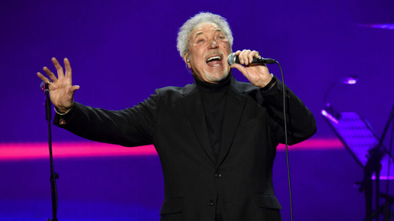 The arena went still — no coughs, no shuffling, no chatter — as Tom Jones repeated the line, his voice carrying decades of love, loss, and lessons learned. This wasn’t just a performance. It was a confession. First released in the late 1960s, I’ll Never Fall In Love Again was already a classic, but in Tom’s hands that night, it became something more — a living, breathing story. Each note trembled with vulnerability yet burned with the strength of someone who’s survived heartbreak and lived to tell it. The lush arrangement wrapped around him like a memory, the melody pulling the crowd through every high and low of love’s dangerous game. Some in the audience wiped away tears. Others simply sat frozen, afraid to break the spell. For those few minutes, it didn’t matter if you’d been in love, lost love, or just dreamed of it — you felt it. And when the final note faded, it left behind a silence that spoke louder than applause. Because some songs don’t just get sung… they get lived.